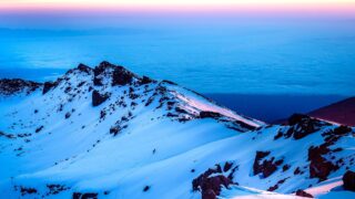 Life Happens Outdoors climbers trekking across snow-covered Kilimanjaro crater toward Stella Point at sunset, with a dramatic purple sky above the summit.