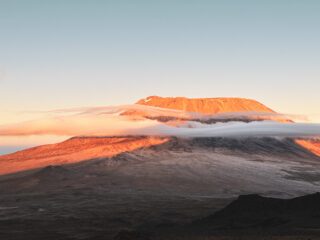Kibo Crater seen from Mawenzi Peak at sunrise on Mount Kilimanjaro, with early lenticular clouds forming around the summit.