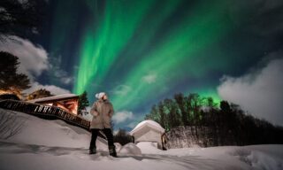 Ghida Arnaout, co-founder of Life Happens Outdoors, standing under the northern lights in Norway at our wild beach accommodation on Senja Island.