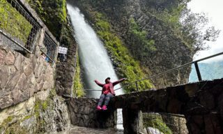 LHO adventurers standing at the base of a powerful waterfall in Baños, Ecuador, surrounded by lush green cliffs.