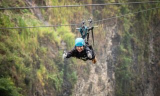 LHO adventurer ziplining into the edge of the Amazon rainforest below Baños, soaring above treetops and deep valleys.