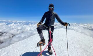 LHO team member striking a tree pose on the summit of Mount Kazbek under clear skies
