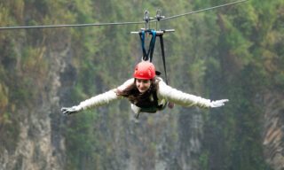 LHO adventurer ziplining into the edge of the Amazon rainforest below Baños, soaring above treetops and deep valleys.