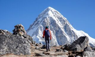 LHO climber trekking to Everest Base Camp during the acclimatisation phase of the Lobuche East climb expedition, with the summit of Pumori visible straight ahead against a clear blue sky.