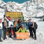 The Life Happens Outdoors team arriving at Annapurna Base Camp, standing by the iconic sign in the snow, during the Annapurna Base Camp Trek.