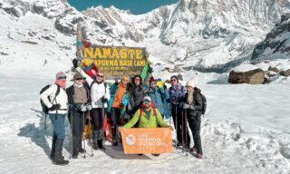 The Life Happens Outdoors team arriving at Annapurna Base Camp, standing by the iconic sign in the snow, during the Annapurna Base Camp Trek.