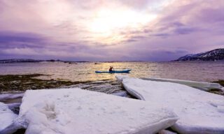 LHO team member kayaking beside blocks of ice on frozen fjords during a Norway northern lights adventure tour.