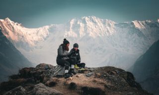 Two Life Happens Outdoors team members enjoying the sunrise with the South Face of Annapurna towering in the background during the Annapurna Base Camp Trek.