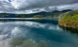 Scenic view of the turquoise crater lake near Quito, surrounded by the dramatic ridges of an Ecuadorian volcano.