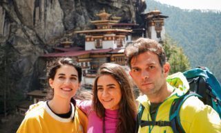 Life Happens Outdoors adventurers posing in front of Tiger’s Nest Monastery in Bhutan on a clear weather day during a Bhutan adventure tour
