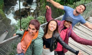 LHO adventurers crossing a suspension bridge high above one of Baños’ waterfalls, with cascading water and jungle views all around.