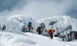 LHO climbers Nada Abanda, Anthony Mezher, and a teammate descending from Cotopaxi crater, surrounded by dramatic glaciers and volcanic terrain in Ecuador.