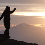 Life Happens Outdoors climber at Karanga Camp on Mount Kilimanjaro, watching a breathtaking sunset with Mount Meru in the distance.