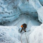Climber descending between towering glacier walls on an abseil, surrounded by shimmering ice formations on the Island Peak climb.