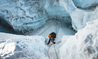 Climber descending between towering glacier walls on an abseil, surrounded by shimmering ice formations on the Island Peak climb.