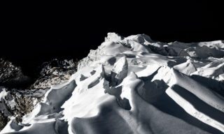 Glaciers of Island Peak jutting into the sky like icy shards, as seen from the summit, with the dark, shadowy waters of Imja Lake looming far below.
