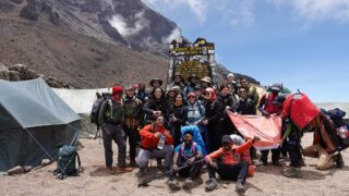 A.T. Kearney team at Lava Tower on Kilimanjaro’s Machame Route, standing under clear skies during their Life Happens Outdoors corporate challenge.