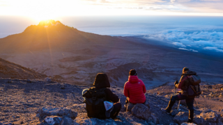 Life Happens Outdoors team watching the sunrise from Stella Point on Mount Kilimanjaro, with the sun emerging above a sea of clouds during their summit ascent.