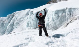 Haneen Alsliman holding her ice axe triumphantly above her head in front of the towering icefall at Crampon Point on the Island Peak climb.