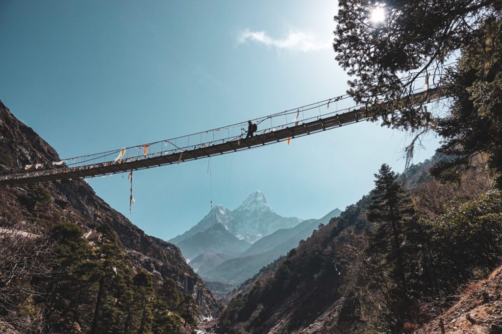 The Life Happens Outdoors team crossing a suspension bridge between Tengboche and Dingboche with Ama Dablam towering in the distance during the Everest Base Camp Trek.