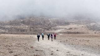 The LHO team walking toward Kibo Hut across Kilimanjaro’s alpine desert saddle, surrounded by mystical fog that obscures the surrounding high peaks.