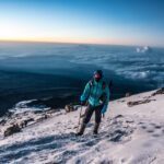 LHOer Omran Antar at sunrise just below Stella Point, with a beautiful purple sky and a sea of clouds covering the savannah plains during the Climb Kilimanjaro Expedition with the Life Happens Outdoors team.
