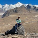LHO Founder and Team Leader Rami Rasamny sitting on a rock with the South Face of Cho Oyu in the background, in spectacular weather during the Gokyo Lakes Trek with the Life Happens Outdoors team.