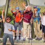 LHOers at the Machame Camp sign at the edge of the rain forest and the short grass vegetation zone on the first day of the Climb Kilimanjaro Expedition on the Machame Route with the Life Happens Outdoors team.