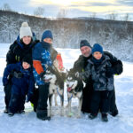 A family with young kids dog sledding during the Find Yourself Under the Northern Lights trip with the Life Happens Outdoors team.
