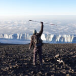 Frederic Sfeir on the summit of Kilimanjaro with the summit glacier in front of him, having climbed it with Retinitis Pigmentosa, during the Climb Kilimanjaro Expedition with the Life Happens Outdoors team.