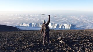 Frederic Sfeir on the summit of Kilimanjaro with the summit glacier in front of him, having climbed it with Retinitis Pigmentosa, during the Climb Kilimanjaro Expedition with the Life Happens Outdoors team.