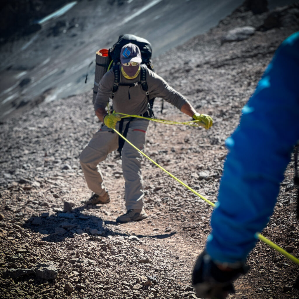 Aconcagua guide Gustavo Caselli assisting Hari Budha Magar, the first double over-the-knee amputee to climb Everest, by pulling him with a rope where the sensors on his prosthetic knees don’t work on uneven surfaces during his successful Aconcagua Expedition with the Life Happens Outdoors team.