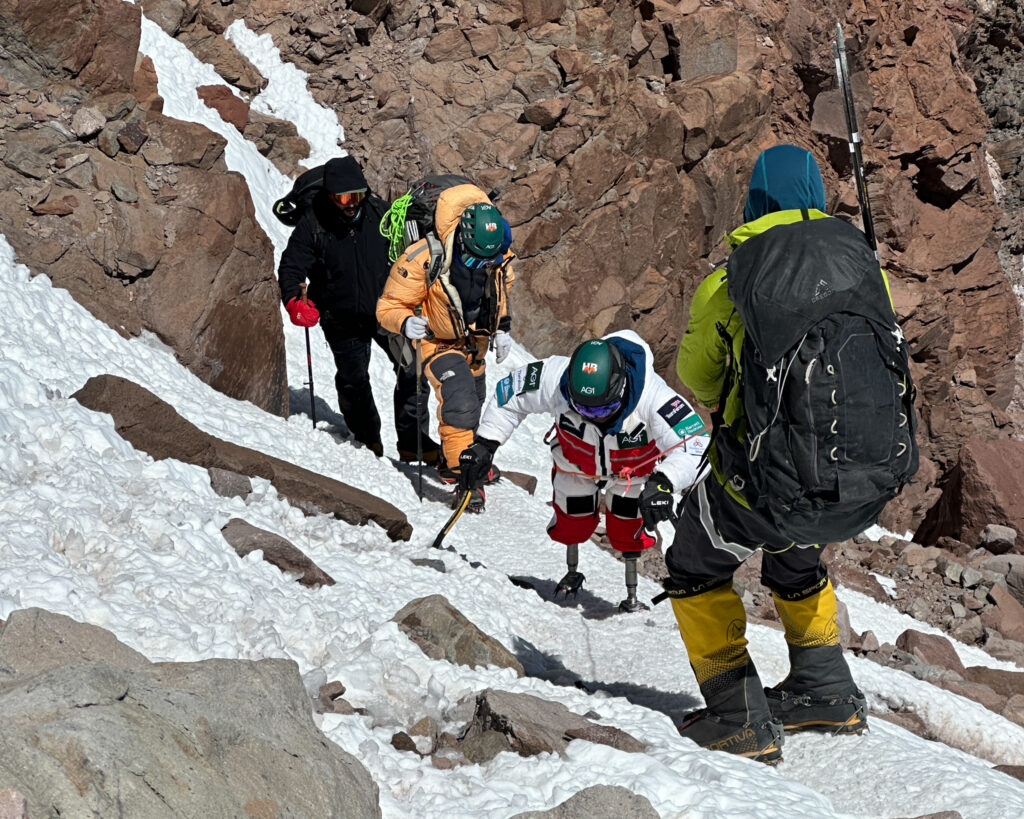 Hari Budha Magar just below the final section on the summit push of Aconcagua. He is using his custom short legs with crampons, assisted by Abiral Rai and Mingma Phortse Sherpa behind him, with Gustavo Caselli on the rope during the Aconcagua Expedition with the Life Happens Outdoors team.