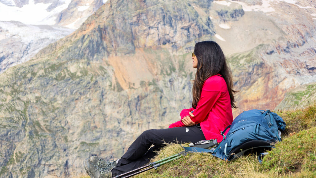 LHO team member at the Grand Col Ferret on the Swiss–Italian border during the TMB hike, with dramatic south face mountain walls in the background.