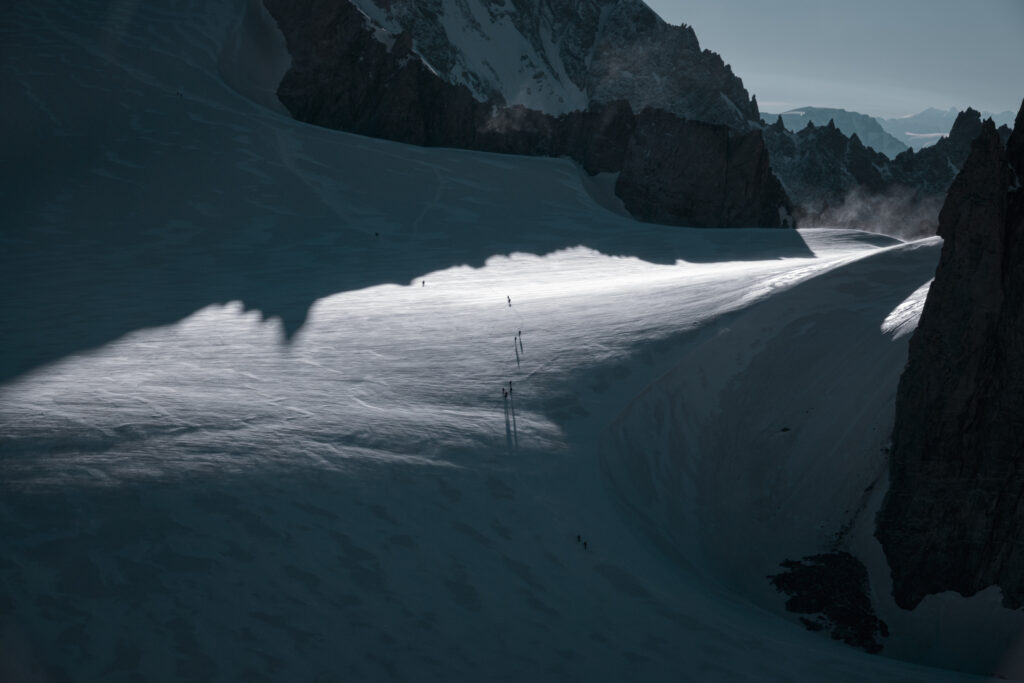 Climbers crossing Glacier du Géant above the Vallée Blanche with dramatic summit shadows creating striking contrast and scale perspective.