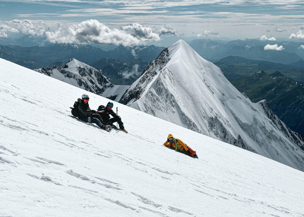 LHO Team Leaders Gino Traboulsi and Hannah Piercy relax with IFMGA guide Pavlos on the slopes of the Dôme du Goûter, descending in perfect conditions with the Aiguille de Bionnassay summit in the background.