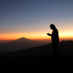 LHO team member watches the sunset from Shira Camp on the Machame Route with Mount Meru visible in the distance during a Kilimanjaro climb.