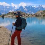 Life Happens Outdoors trekker standing at Lac Blanc on day one of the Tour du Mont Blanc hike, with the Mont Blanc summit and full Mont Blanc massif visible across the valley under a clear blue sky.