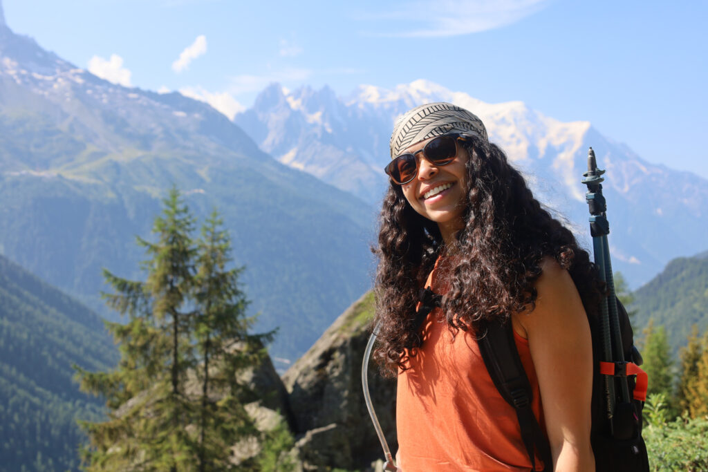 Smiling Life Happens Outdoors trekker at Col des Posettes with Mont Blanc towering in the background on a clear day during the Tour du Mont Blanc route to Col de Balme