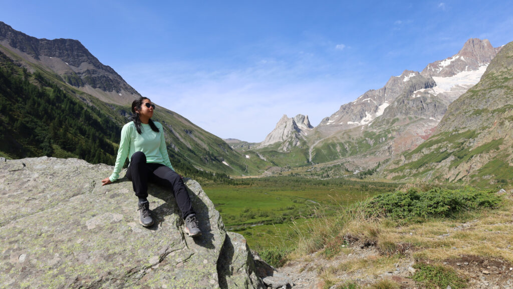 Life Happens Outdoors trekker resting on a rock above Italy’s Val Veny with Col de la Seigne visible ahead on the French-Italian border during a clear blue sky day on the Tour du Mont Blanc