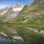 Life Happens Outdoors group hiking past alpine lakes in Italy's Val Veny on the Tour du Mont Blanc route to Col de la Seigne under clear blue skies