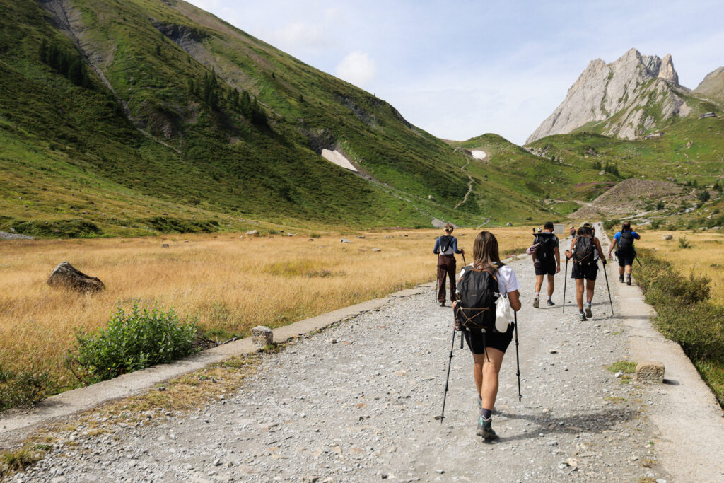 Life Happens Outdoors team trekking through lush green Val Veny toward Col de la Seigne on the Italian section of the Tour du Mont Blanc trail with Mont Blanc rising behind.