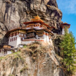Panoramic view of Tiger’s Nest Monastery perched dramatically on a cliffside in Bhutan, surrounded by lush forest and misty mountain air.