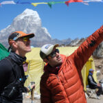 Rami Rasamny at Ama Dablam Base Camp explaining mountain conditions to a visiting trail runner amid uncertain weather and climbing delays.