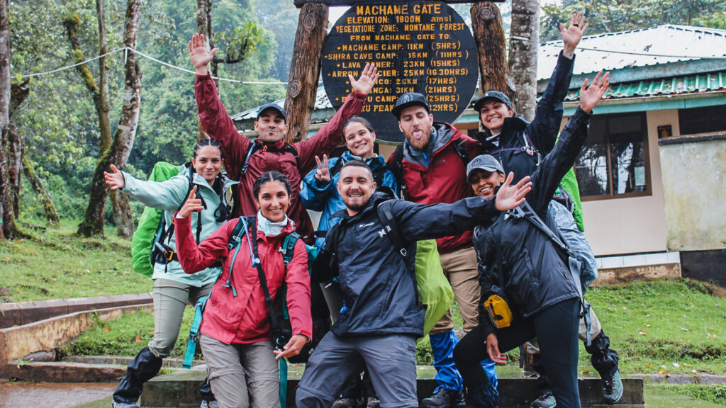 LHO team posing at the Machame Gate sign, marking the start of their Kilimanjaro climb via the Machame Route on their hiking mount Kilimanjaro adventure.