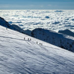 LHO climbers descending Monte Rosa in clear weather, silhouetted against a vast sea of clouds filling the valley below, showcasing an epic alpine landscape.