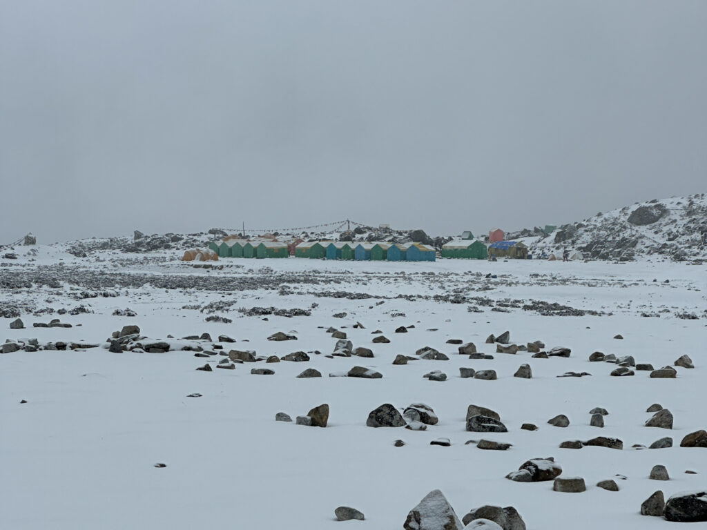 Ama Dablam Base Camp blanketed in snow during unseasonably heavy weather, with tents partially buried and visibility reduced across the camp.