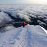 Life Happens Outdoors team climbing the ridge of Cotopaxi at sunrise with a glowing horizon above and a sea of clouds stretching across the valleys below