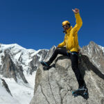 Life Happens Outdoors guide standing on the summit of Petit Flambeau with Mont Blanc rising majestically in the background under a clear alpine sky