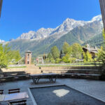 View of the Mont Blanc massif from the garden of RockyPop Hotel, with alpine peaks in the distance and outdoor seating in the foreground.